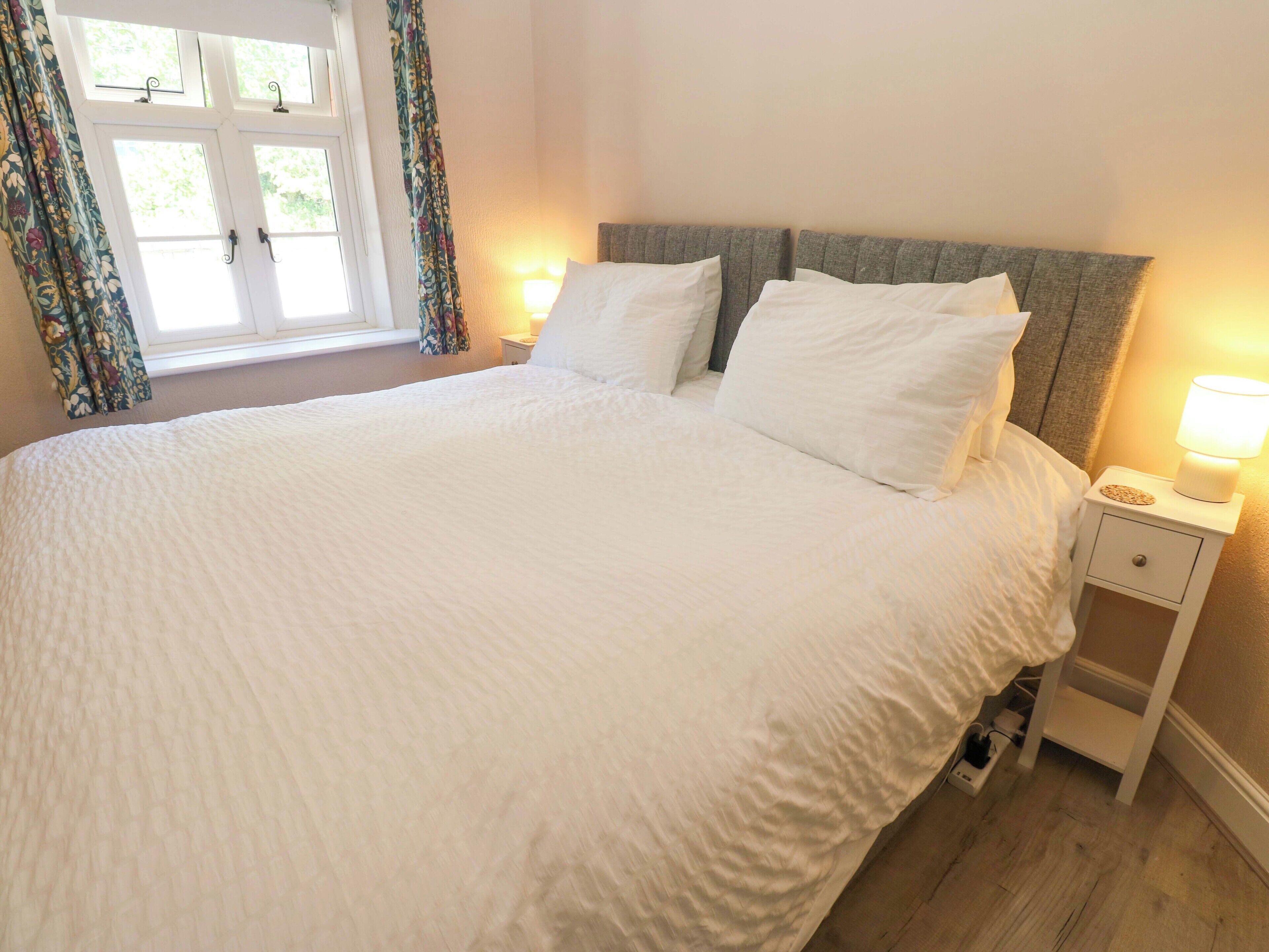 Una cama bien hecha con cabecera gris, ropa de cama blanca y dos lámparas de noche.