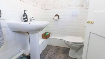 Un baño pequeño y limpio, con un lavamanos blanco, inodoro y un pequeño cubo de basura.
