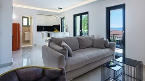 A modern living room with a grey sofa, a dining area, and a kitchen in the background. - Villa Aea Del Mare: Luxury 5BR Villa with Pool, Wellness & Sea Views - Sleeps 12 (Okrug Gornji)