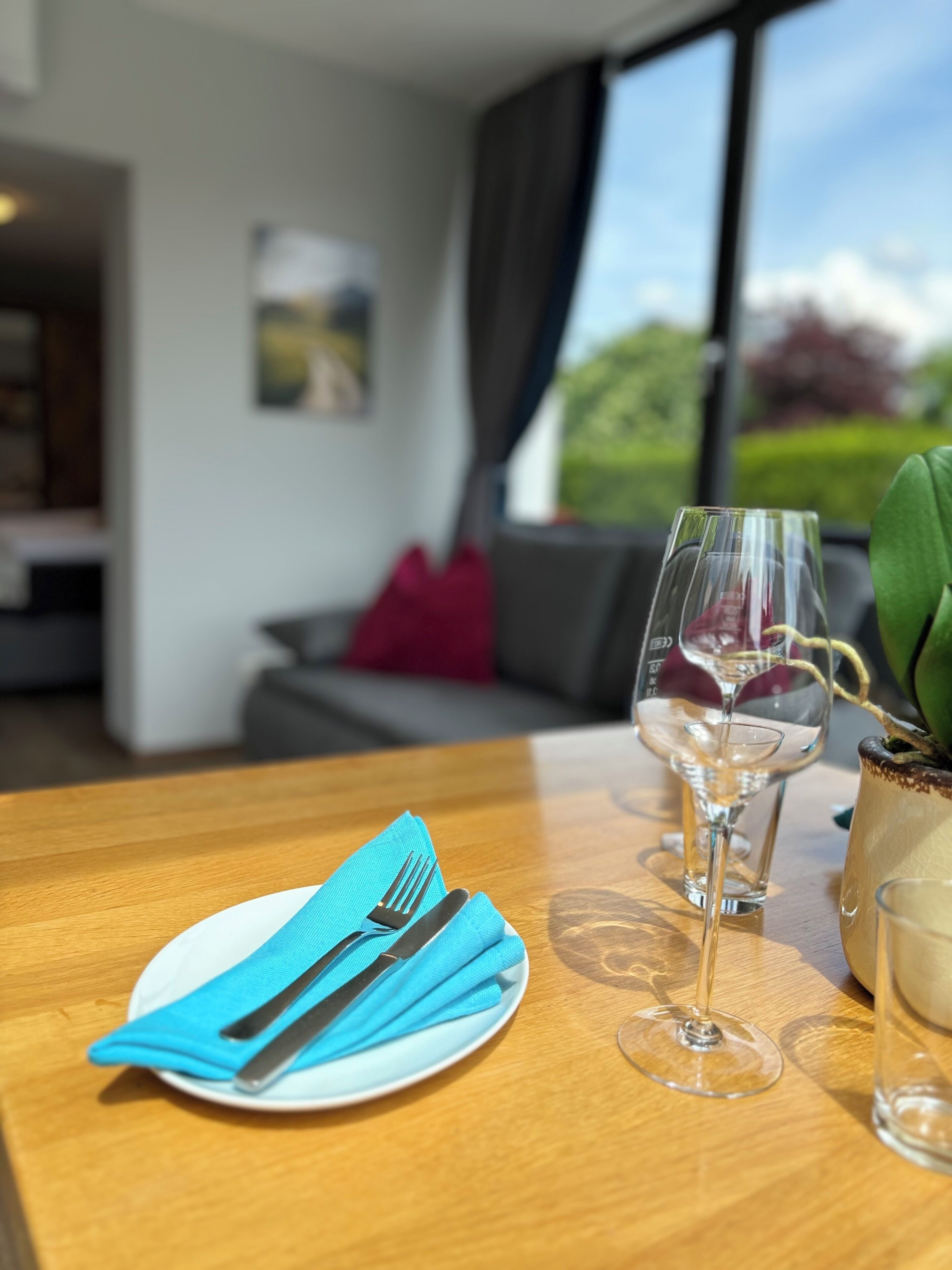 A dining table with a blue napkin, cutlery, and two wine glasses.