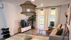 A modern living room with a dining area, a sofa set, a TV, and a large window with curtains. - La Tejita Vida by Be Happy Sotavento Suites (La Tejita)