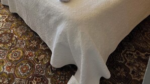 Un letto rifatto con due asciugamani arrotolati, un tappeto decorato e una finestra con tende.