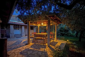 Un patio al aire libre con suelo de piedra, mobiliario de madera y una estructura de pérgola.