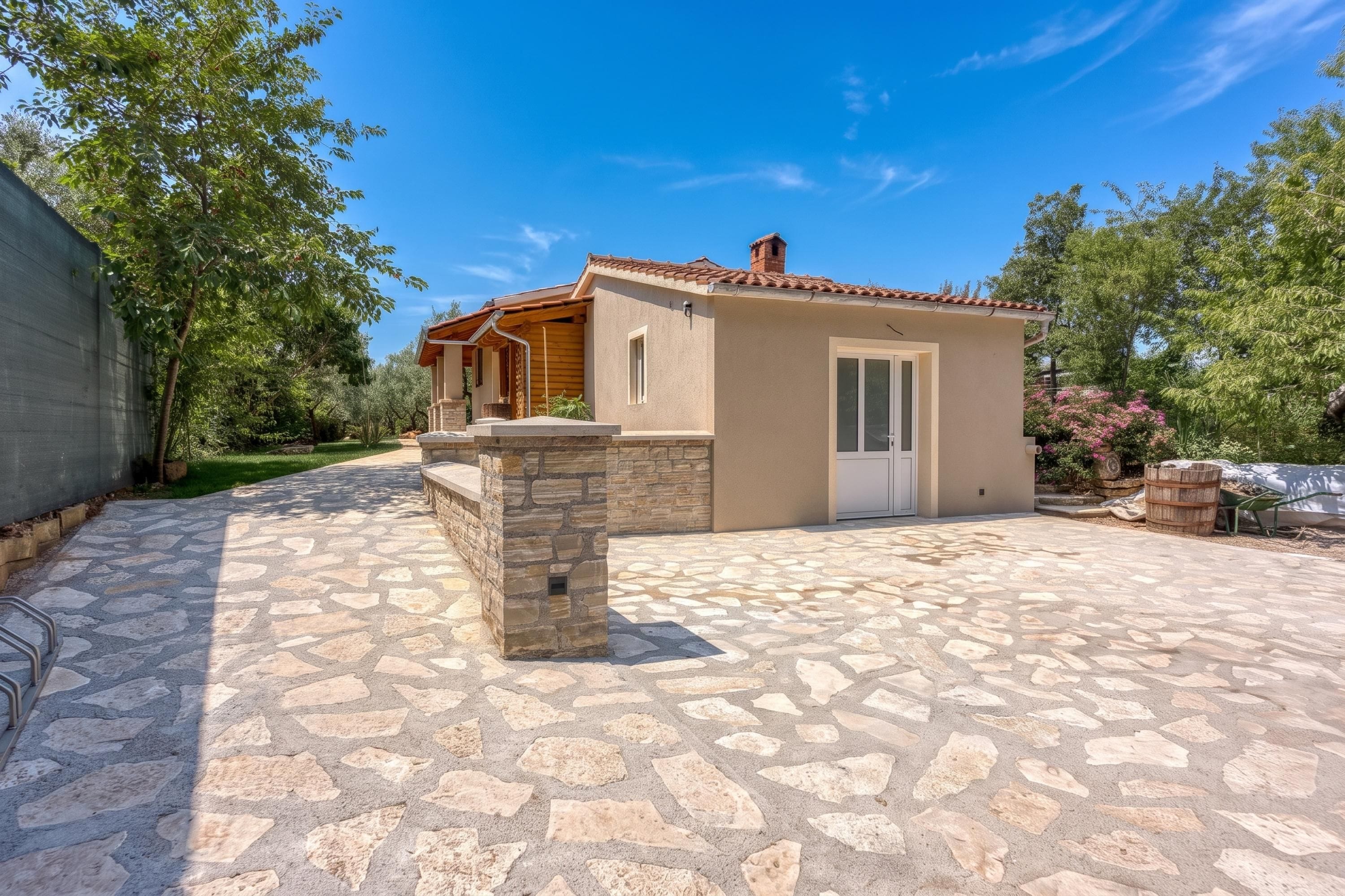 Una casa con un patio in pietra, un pergolato in legno e un piccolo giardino.