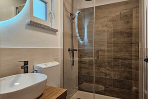 A bathroom with a white sink, a glass shower enclosure, and a wooden vanity.