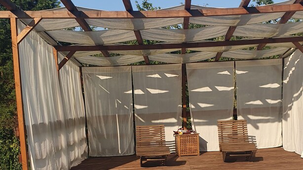 A covered outdoor seating area with two wooden benches, a small table, and a pool in the foreground. - In the capital of the Langhe cottage with pool and garden (Ricca)