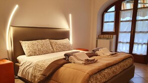 A neatly made bed with a headboard, a bedside table, and a window with curtains. - In the capital of the Langhe cottage with pool and garden (Ricca)