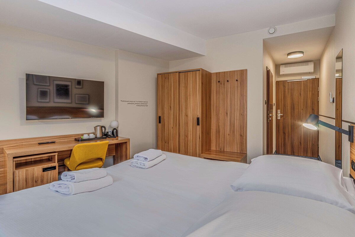 A hotel room with a bed, a desk with a chair, a television, and a wardrobe.