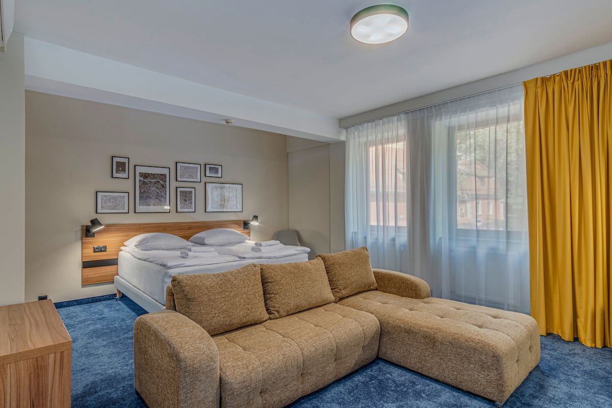 A hotel room with a bed, a sofa, a desk, and a window with curtains.