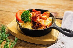 A skillet with scrambled eggs, bacon, and a tomato garnish on a wooden board. - Tulip Hotels - Wroclaw Centre (Wroclaw)