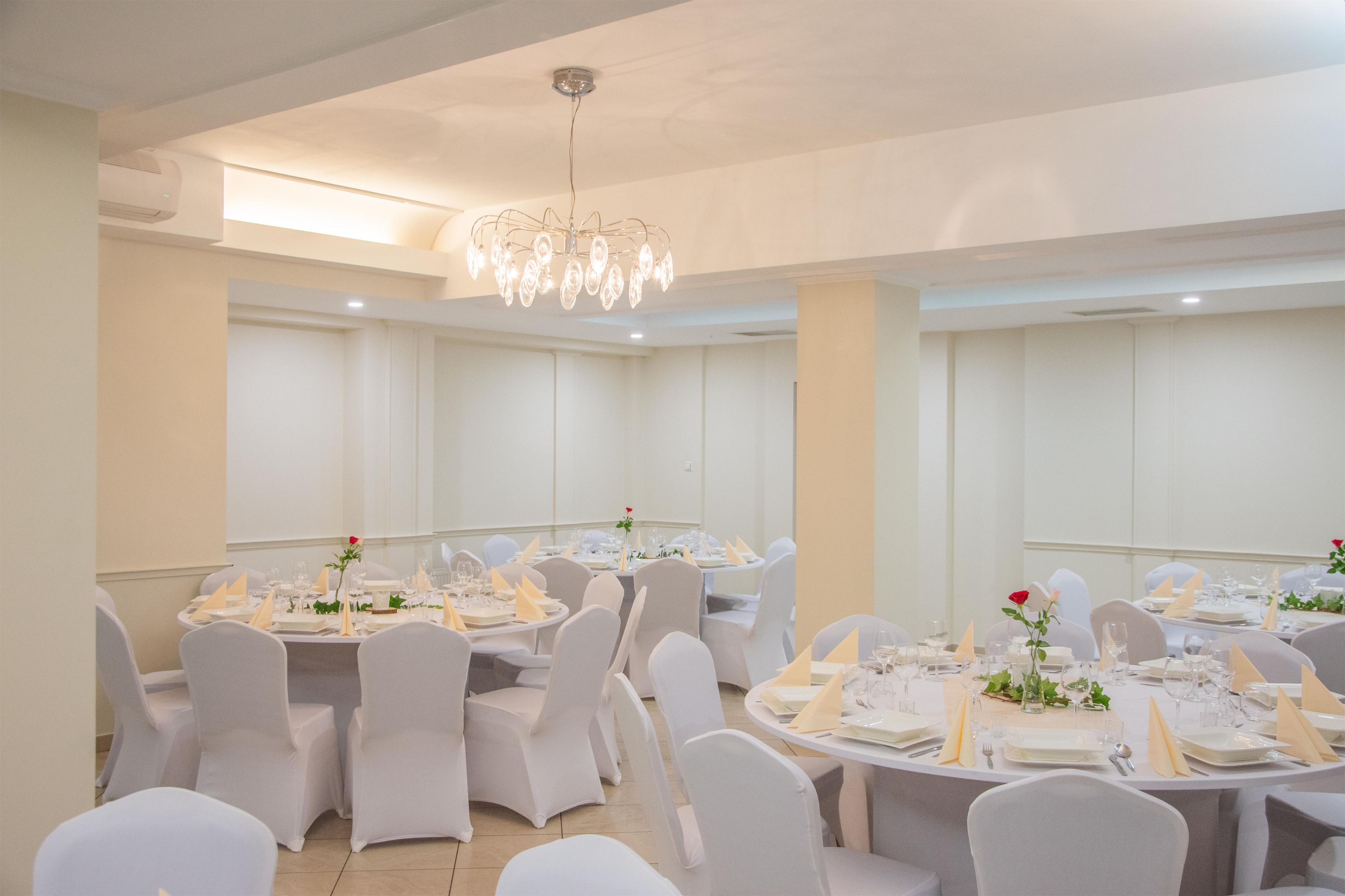 Un salón de banquetes con mesas redondas, sillas blancas y una araña de cristal.