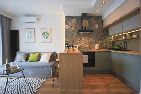 A modern kitchen with a central island, a grey sofa with cushions, and a patterned rug.
