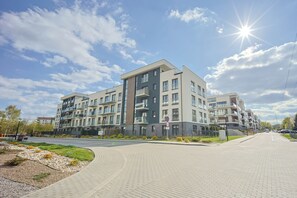 A multi-story residential building with balconies, a paved walkway, and a clear sky.