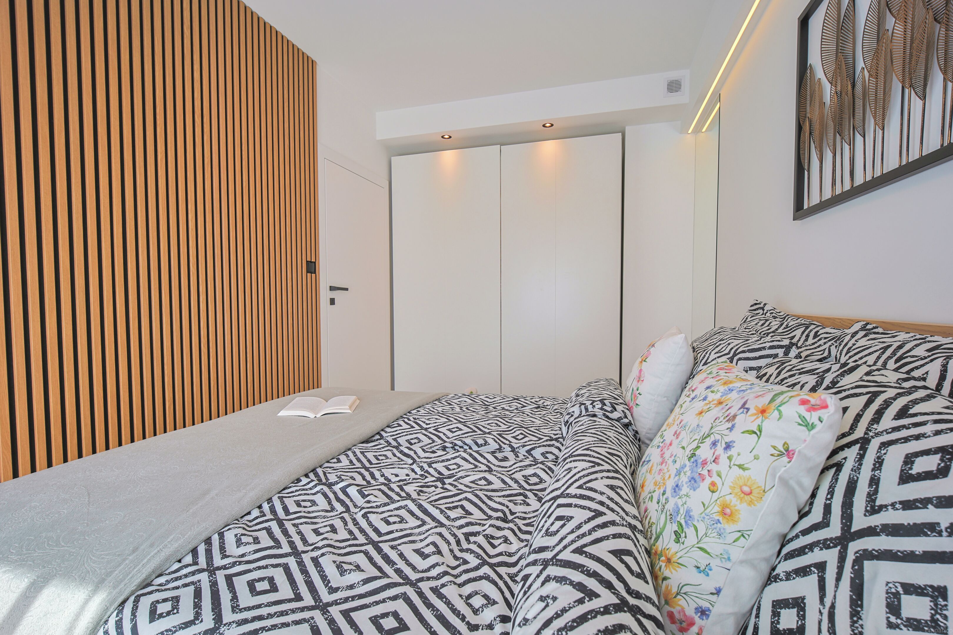 A bedroom with a bed, a wooden slat wall, a wardrobe, and a framed artwork.