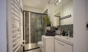 A modern bathroom with a glass shower enclosure, a toilet, a sink with a mirror, and a towel rack. - Mala Poleska - Cozy Garden Apartment Near Jasna Góra / Parking & Wi-Fi (Częstochowa)