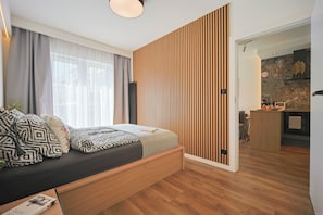Ein modernes Schlafzimmer mit Bett, Vorhängen, einer Holzwand, einer Küchenzeile und einem Esstisch.