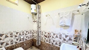 Une salle de bain équipée de toilettes, d’un lavabo, d’une douche et dont les murs sont décorés de carreaux.