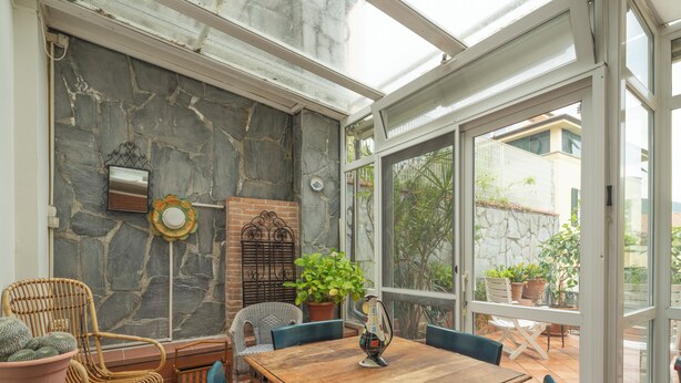 Un patio iluminado por el sol con una mesa de madera, sillas de mimbre y plantas en macetas.