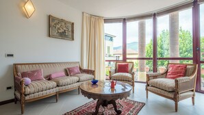 Una sala de estar con sofá, sillones, una mesa de centro y un ventanal con vistas a zonas verdes y edificios.