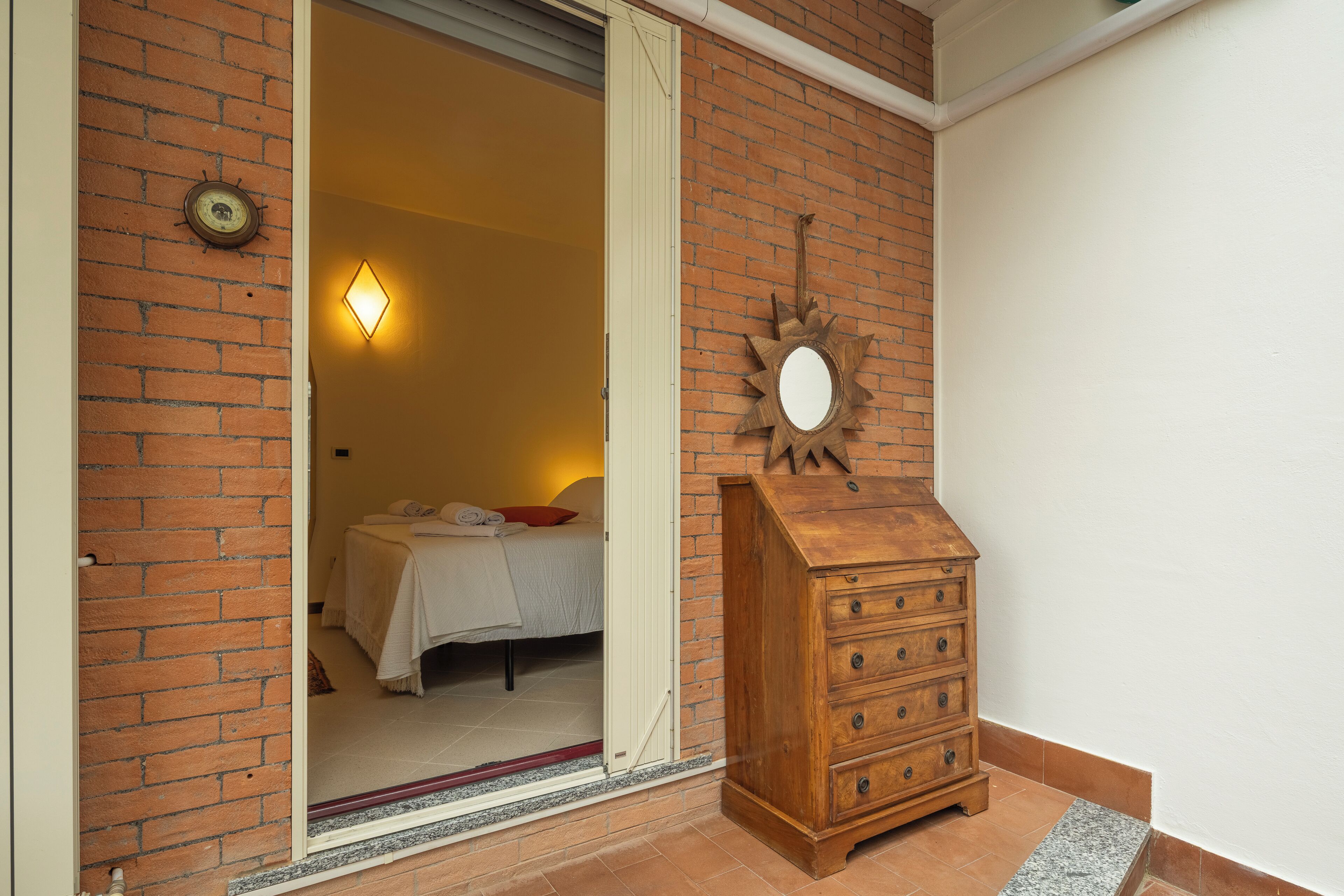 Een kamer met een bed, een houten dressoir, een wandklok en een deur naar een andere kamer.
