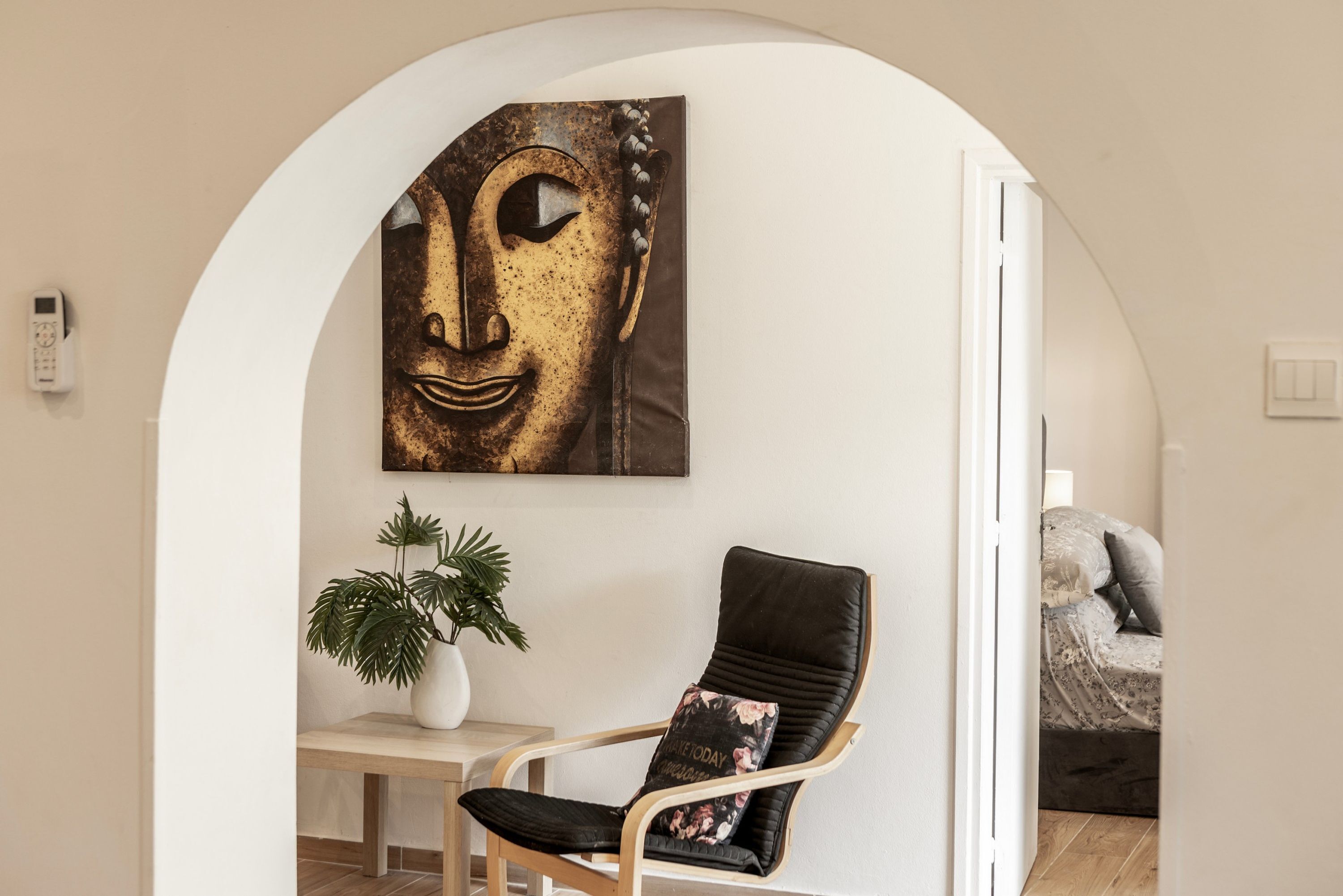 A room with a modern chair, a potted plant, and a wall-mounted artwork.