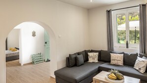 Una sala de estar moderna con un sofá seccional gris, una mesita con un frutero y una ventana con cortinas.