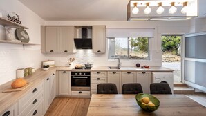 Una cocina moderna con armarios blancos, encimera de madera, horno empotrado, lavamanos y comedor con mesa y sillas.