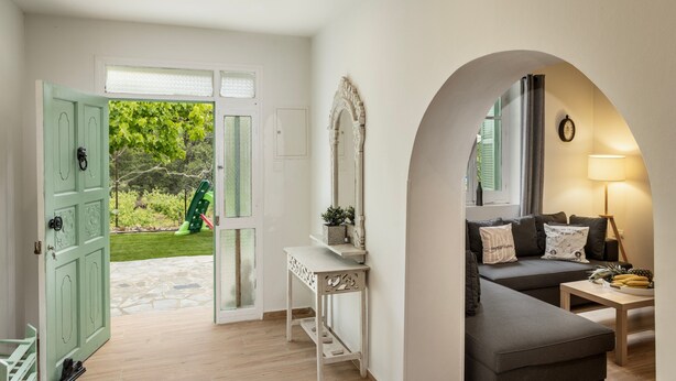 Una sala moderna con un sofá gris, una consola blanca y una puerta verde que da a un jardín.