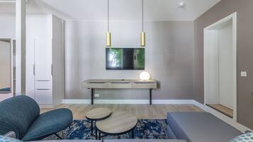 Una sala moderna con un sofá, dos mesitas, un televisor montado en la pared y lámparas colgantes.