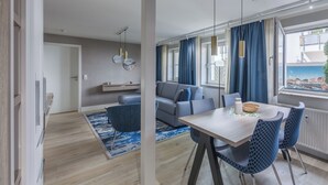 Ett modernt vardagsrum med en soffa, ett matbord med stolar och utsikt över staden genom stora fönster.