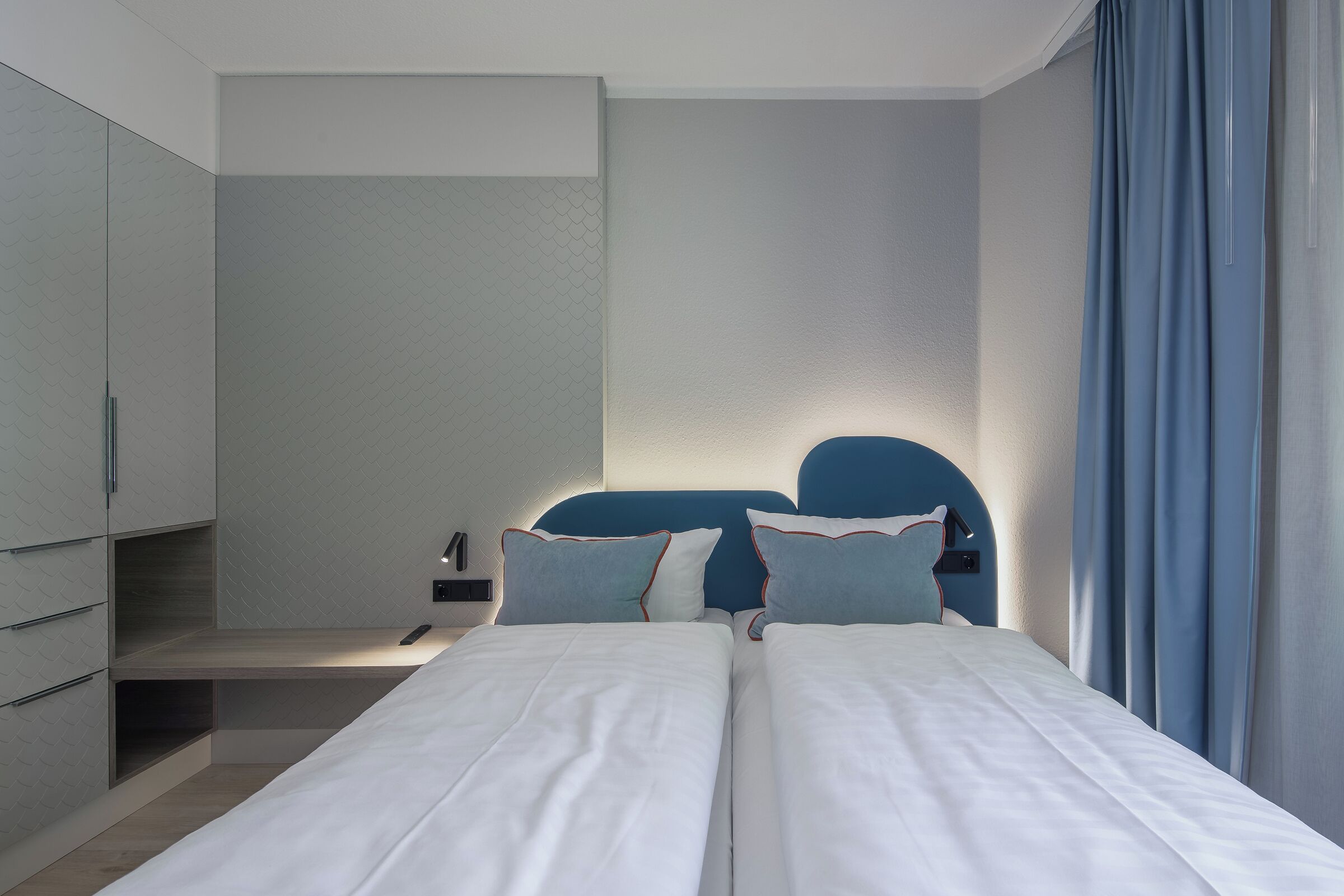 A modern hotel room with two beds, a wardrobe, and a nightstand.