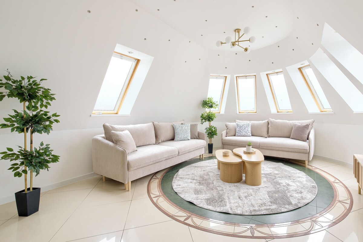 A modern living room with two sofas, a coffee table, and a TV. There are skylights and a ceiling light fixture.