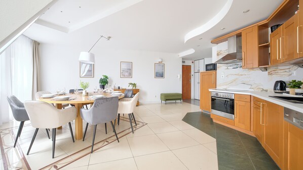 A modern kitchen with wooden cabinets, a built-in oven, and a dining area with a round table and chairs. - Sun & Snow Port I (Kolobrzeg)