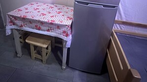 Una cocina compacta con refrigerador, una pequeña mesa de madera con mantel floral y un banco.