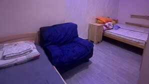 Una habitación pequeña, con poca luz, que tiene un sofá azul, una mesa de madera y una cama individual.