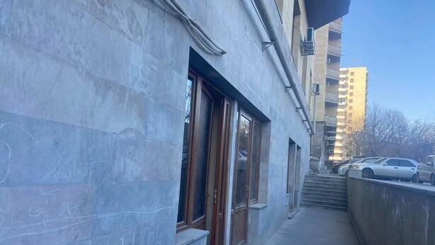 Una calle urbana estrecha con un edificio que tiene ventanas grandes y una entrada visible.