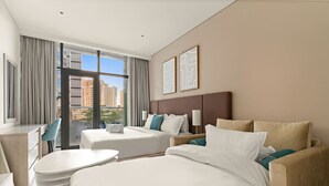 A hotel room with a large bed, a sofa, a desk, and a chair. There is a window with curtains, and two framed pictures on the wall. - FIRST CLASS | Studio | Palm Paradise (Dubai)