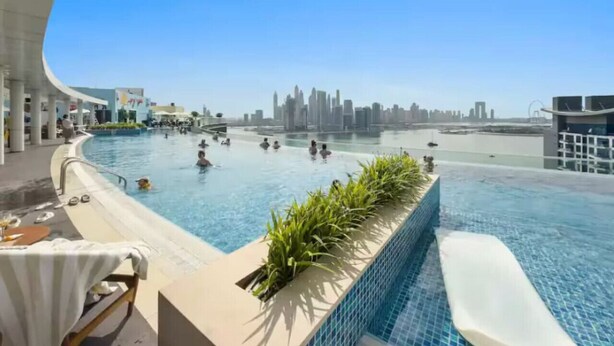 A rooftop infinity pool with a city skyline view, surrounded by lounge chairs and a poolside bar. - FIRST CLASS | Studio | Palm Paradise (Dubai)