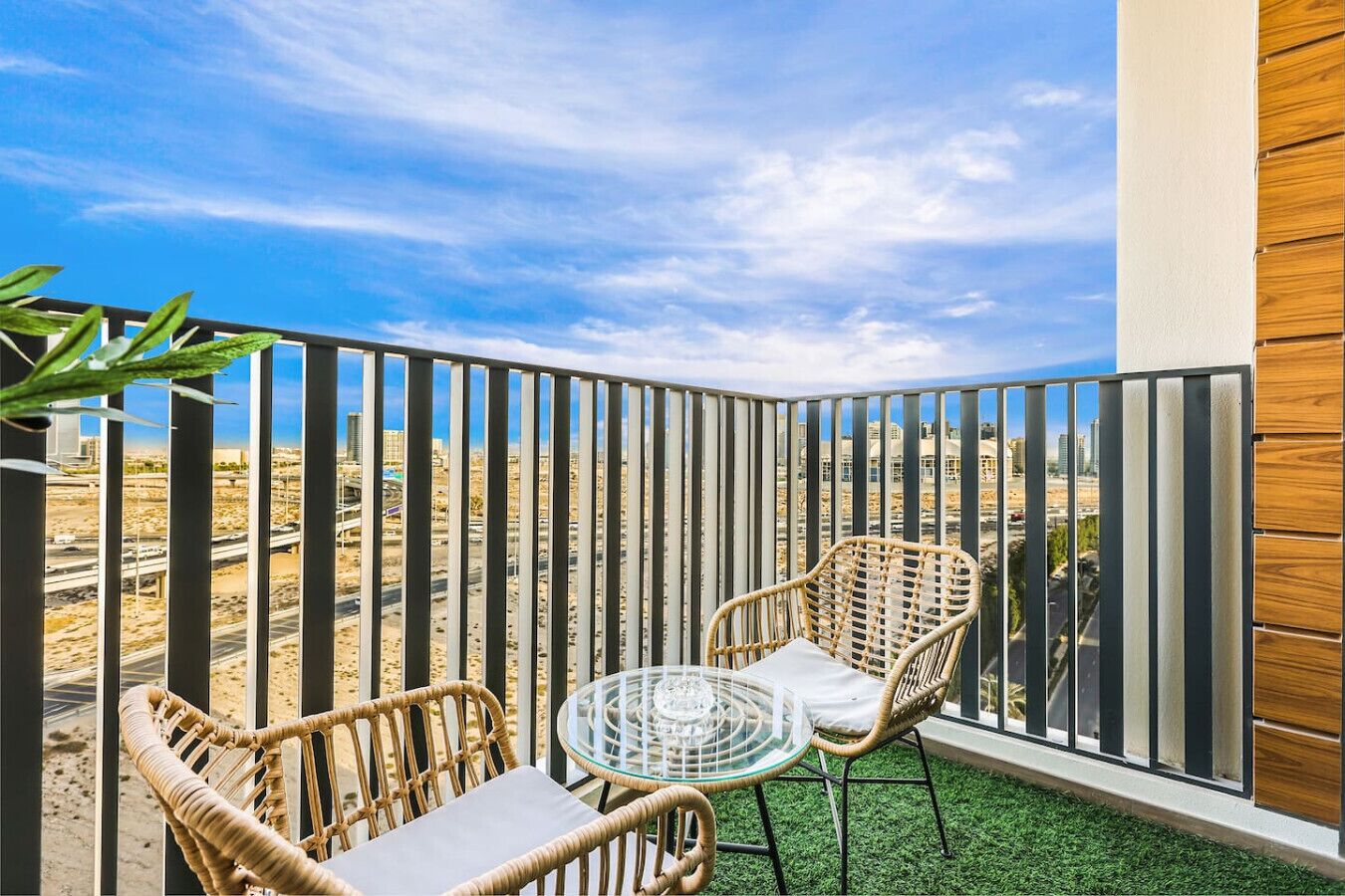 Ein Balkon mit Korbmöbeln und einem Glastisch, mit Blick auf eine Wüstenlandschaft.