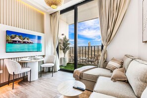 A modern living room with a flat-screen TV, a sofa, a coffee table, and a balcony with a view of the ocean. - FIRST CLASS | Studio | Unwind in Style (JVC)