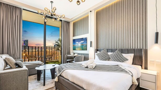 Una habitación de hotel moderna con una cama grande, una zona de estar con una mesa y un balcón con vistas a la ciudad.