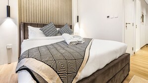 Una habitación de hotel moderna con una cama grande, cabecera de madera y una manta decorativa.