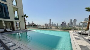 Una piscina en la azotea con vistas al horizonte de la ciudad, rodeada de sillones de descanso y palmeras.