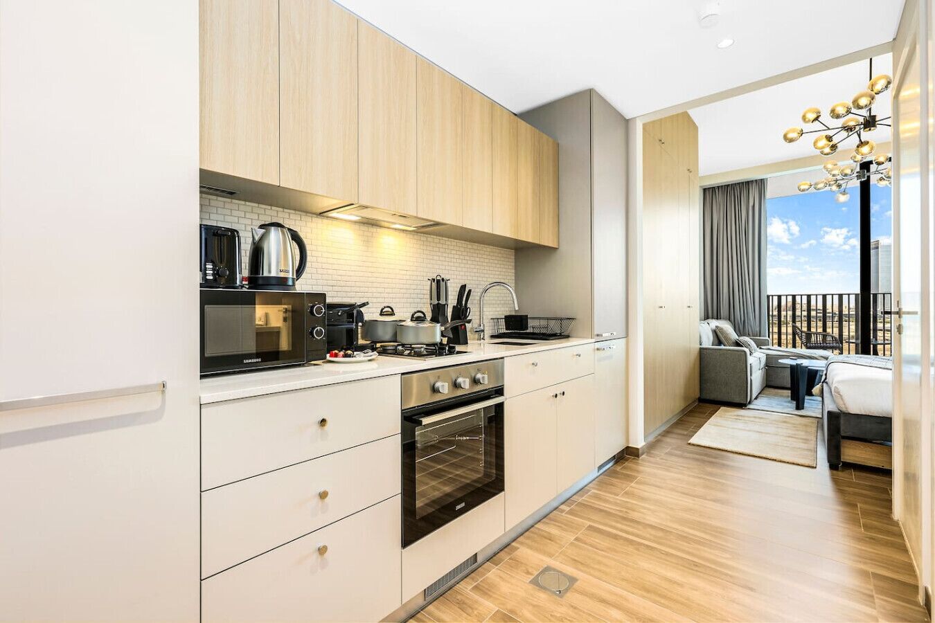 A modern kitchen with white cabinets, a built-in oven, and a stove. There is a balcony with a sofa and a dining table.