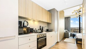 Una cocina moderna con armarios blancos, horno empotrado y estufa. Cuenta con un balcón con sofá y mesa de comedor.