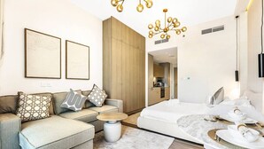 Une chambre d’hôtel moderne avec un canapé, une table basse ronde, un lit avec une tête de lit blanche et un coin repas doté d’une table en marbre.