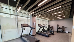 Une salle de sport moderne équipée de tapis de course, d’appareils de musculation et d’une grande fenêtre laissant entrer la lumière naturelle.