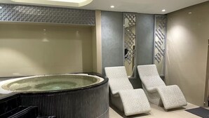 Un'area benessere con vasca idromassaggio, due poltrone relax e una scala che conduce a un livello superiore.