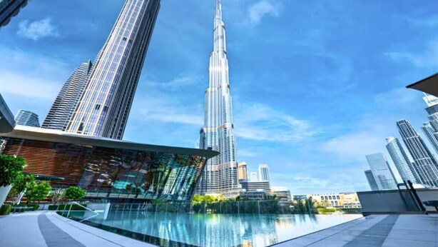 Paesaggio urbano moderno con un grattacielo imponente, un elemento d'acqua riflettente e circostanti edifici di grandi dimensioni.