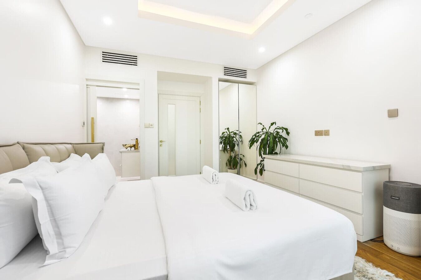 Une chambre à coucher moderne avec un grand lit, une table de chevet, un miroir, une armoire et une poubelle.